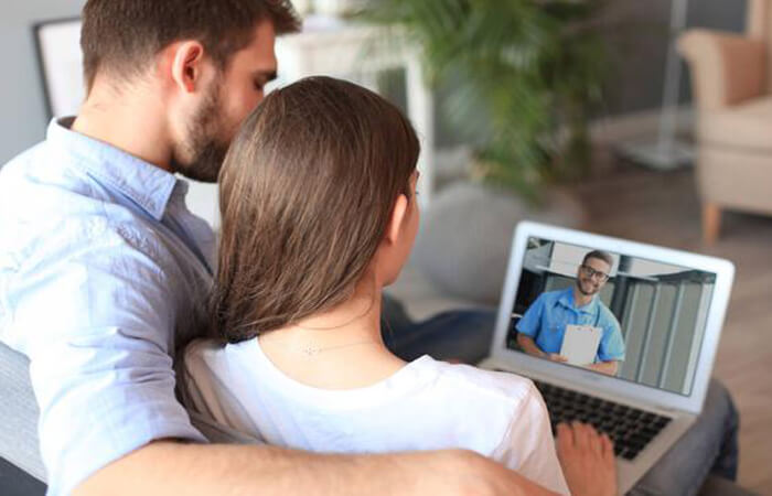 Picture of a happy couple having a video conference with their fertility doctor in Costa Rica.  The couple is smiling and looking into a laptop computer.