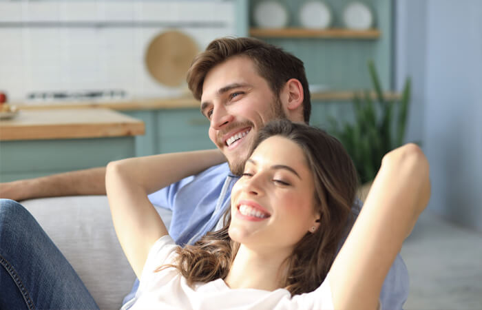 Picture of a young couple sitting on a couch and smiling.