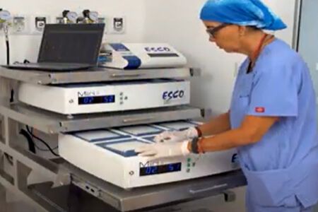 Picture of the interior of a fertility laboratory, representing the capabilities of an IVF fertility center.  The person is wearing white gloves, a blue head covering and a blue smock.