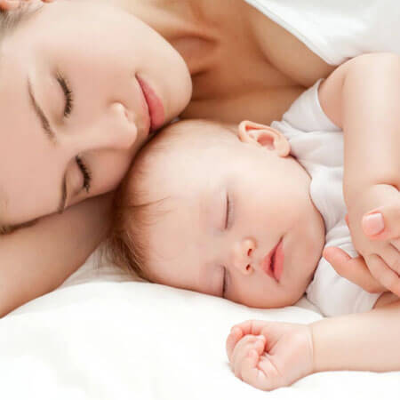 Picture of a woman sleeping with her baby.  Both the mother and baby are sleeping with their face to the camera.